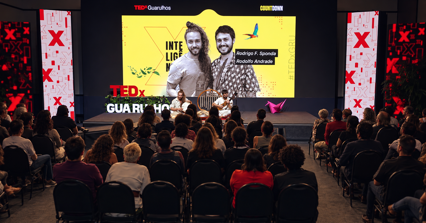 Rodrigo F. Sponda e Rodolfo Andrade se apresentando no palco do TEDxGuarulhos para o público sentado